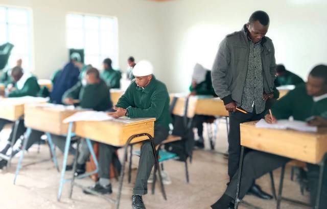 Students sitting an exam while a teacher looks on